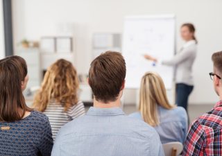Rear View of Young Office Workers in Casual Outfits Listening to a Top Manager Explaining Something Using Illustrations.